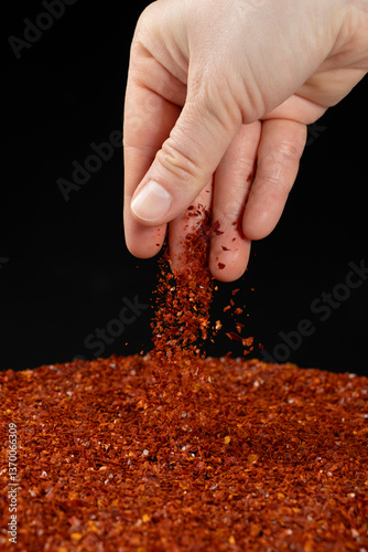 Hand pouring dried ground red chili peppers, natural seasoning, close-up