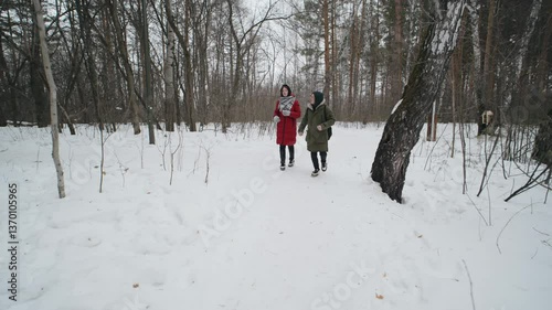 Two individuals stroll together on a snowy path surrounded by trees during winter