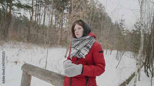 A girl dressed in a bright winter coat sits on a log in a snowy forest