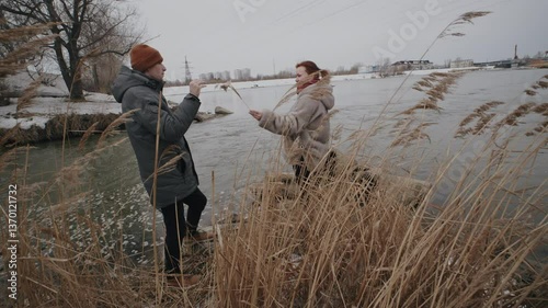 Two people walking by the riverbank on a cold winter day observing the icy landscape