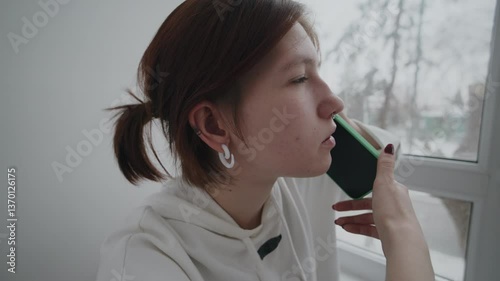 Young woman talking on the phone while looking out the window during a snowy winter day