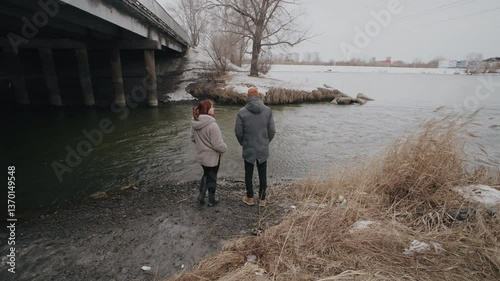 Couple enjoying winter stroll by the riverbank surrounded by reeds in a serene natural setting during the snowfall