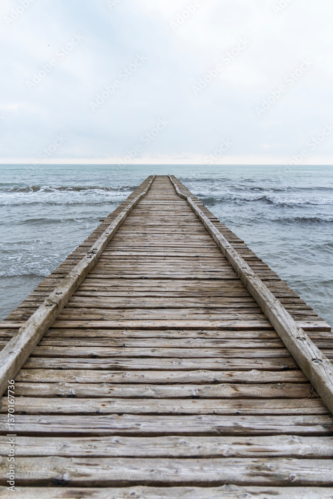 Wooden pier leading to the Adriatic Sea on a cloudy autumn beach in Italy Wooden pier leading to the Adriatic Sea on a cloudy autumn beach in Italy