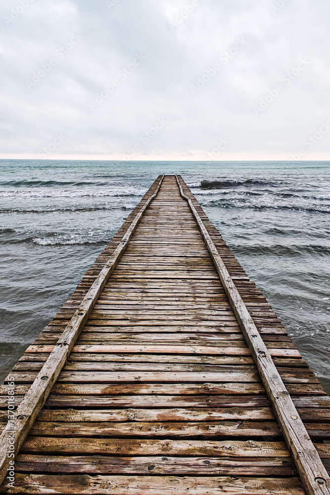 Fototapeta premium Wooden pier leading to the Adriatic Sea on a cloudy autumn beach in Italy