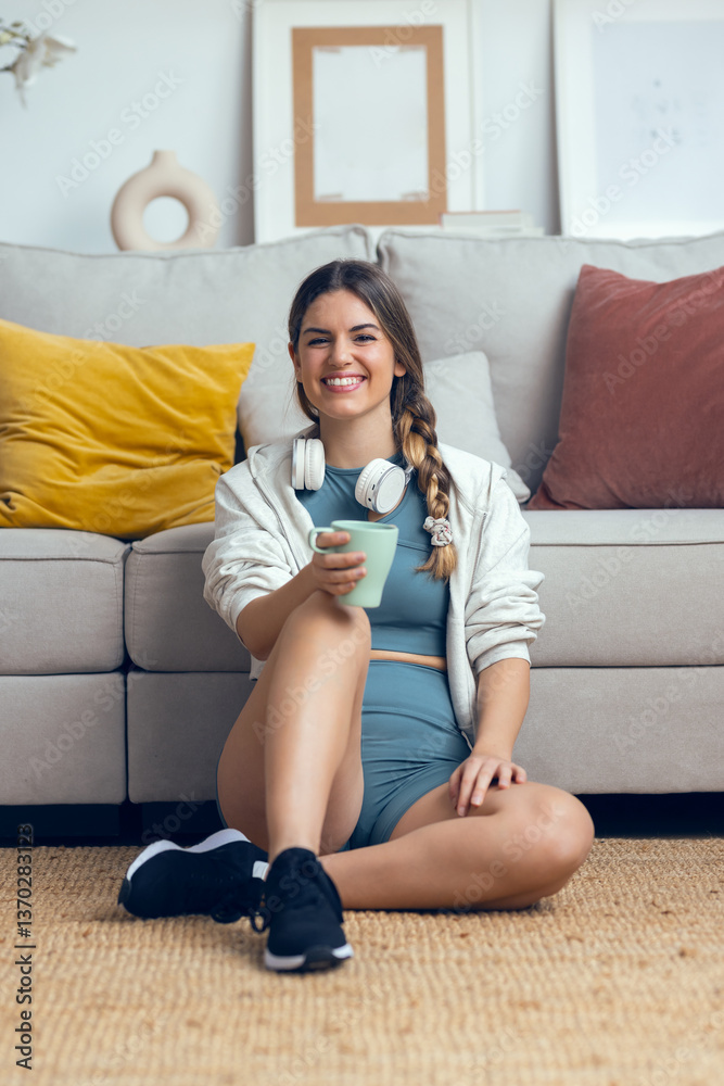 Obraz premium Sporty woman drinking coffee while looking at camera sitting on the floor at home