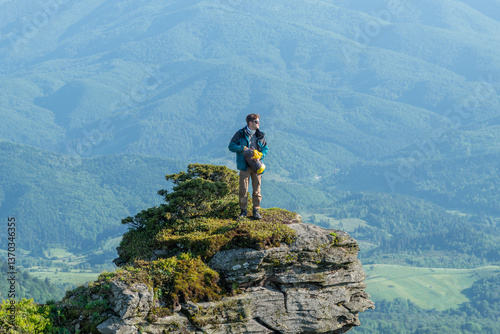 A man hiker puts clothes into a duffel bag while standing on the edge of a rocky mountain peak at sunset, with a breathtaking view of the landscape. photo