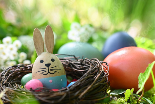 Kleines Nest mit Osterdeko, im Hintergrund drei bunte Eier	