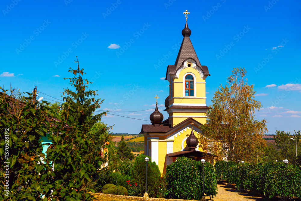View of monastery in village Tipova from Moldova. Serene church stands tall against a vibrant blue sky, its pale yellow facade a beacon in the countryside