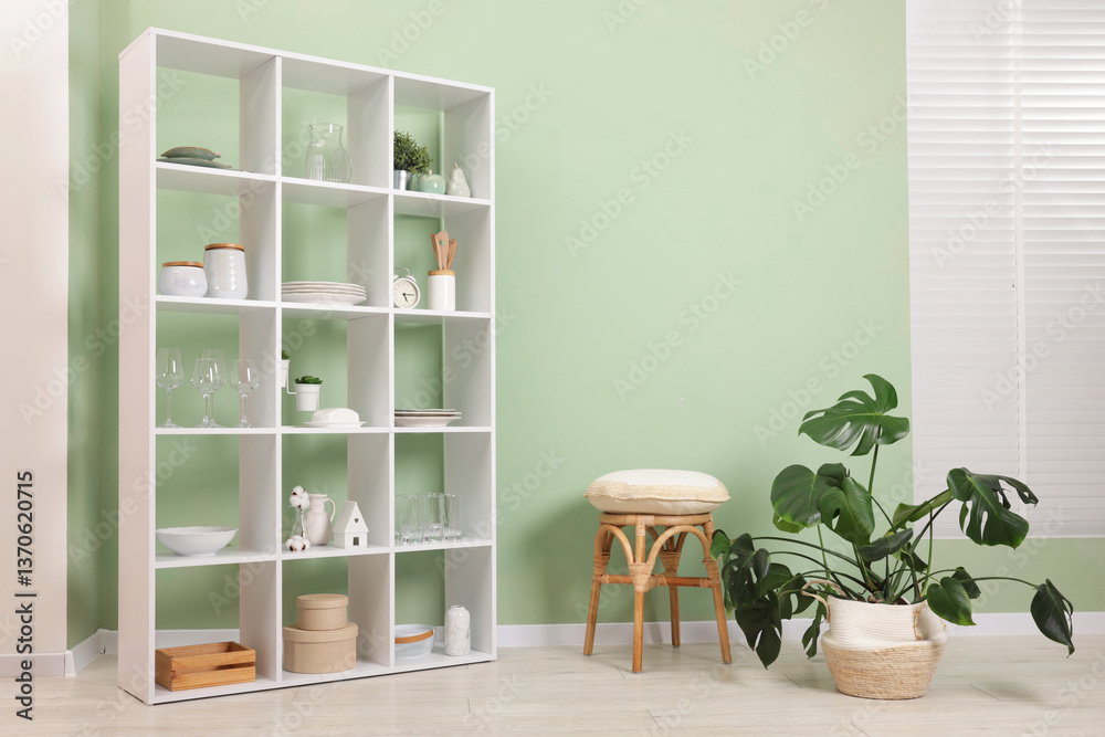 Fototapeta premium Shelving unit with dishware near olive wall indoors. Space for text