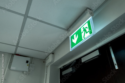 Industry-standard illuminated Fire Exit sign seen at the fire escape and emergency exit doors within a typical hospital. An alarm system can be seen in the background.