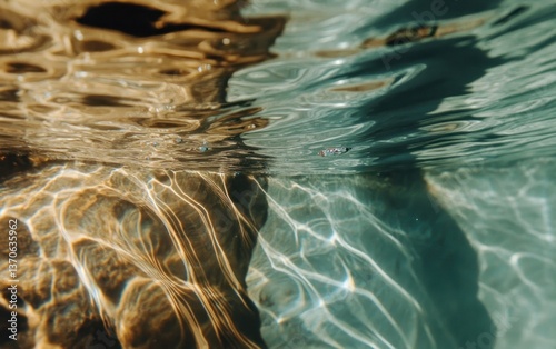 Abstract underwater image of shimmering water with golden and teal hues. Light plays on the surface creating patterns and textures. The photograph is taken from an underwater perspective, showing the