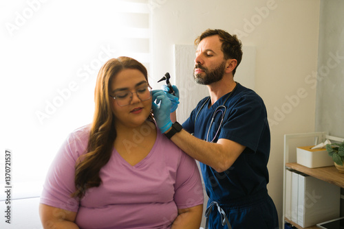 Male doctor using an otoscope examining ear of female patient during medical consultation in doctor's office
