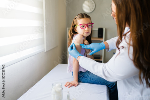 Pediatrician applying bandage to girl's arm after administering a vaccine in a medical clinic, providing healthcare and immunization