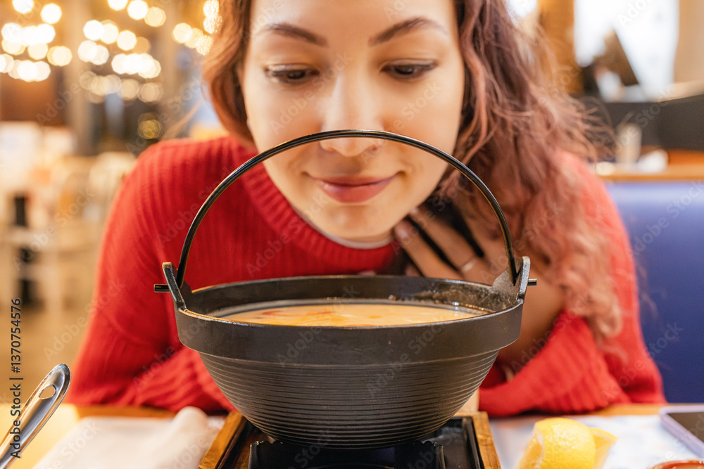 Customer savoring the delightful aroma of hot soup served in an individual pot at a cozy Japanese restaurant, enjoying a traditional meal