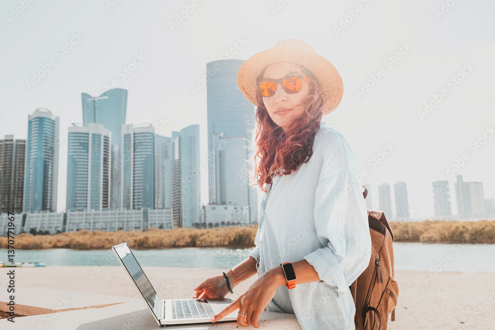 Freelancer working on a laptop while soaking in the stunning views of modern skyscrapers in Abu Dhabi's vibrant skyline