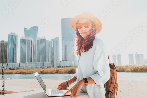 Obraz na płótnie Freelancer working on a laptop while soaking in the stunning views of modern skyscrapers in Abu Dhabi's vibrant skyline w salonie