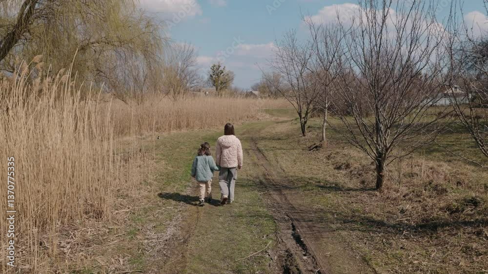 Two young girls walk along a grassy path in the countryside on a bright spring day, enjoying peaceful time in nature near a lake