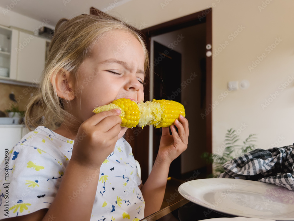 Little girl eating corn on the cob sitting at the table in the kitchen Little girl eating corn on the cob sitting at the table in the kitchen