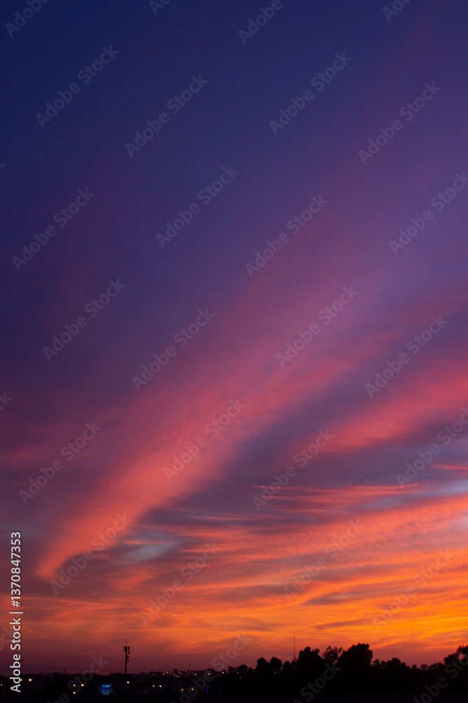 Fototapeta premium Breathtaking sunset with vibrant hues of orange, red, and purple painting the sky. The silhouetted trees and distant antenna create a serene and dramatic evening landscape