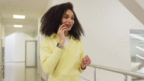 Wallpaper Mural Beautiful African American woman walking in bright modern office corridor while talking on smartphone. Engaging in conversation while gesturing expressively. Communicating remotely with client. Torontodigital.ca