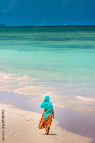 local girl dressedIn traditional clothes walking on the beach of jambiani, zanzibar, tanzania