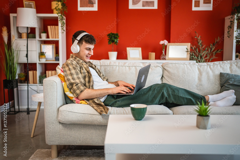 Obraz premium cheerful young man with headphones lying down on sofa and use laptop