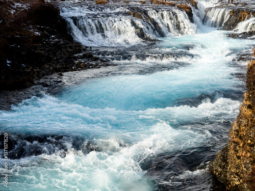 Bruarfoss Waterfall, Iceland: Crystal-clear turquoise water cascades over rugged volcanic rock, creating a striking contrast between icy blue and dark basalt
