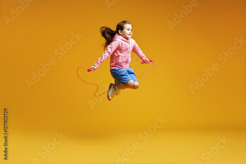 Foto Cute little girl with jump rope on yellow background