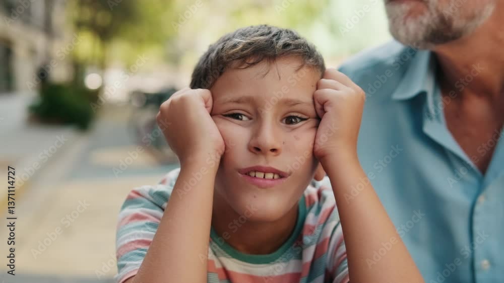 Grandfather kisses grandson on head. Grandson looks at camera with a bored expression. Family bonding outdoors. Grandfather kisses grandson on head. Grandson looks at camera with a bored expression. Family bonding outdoors.