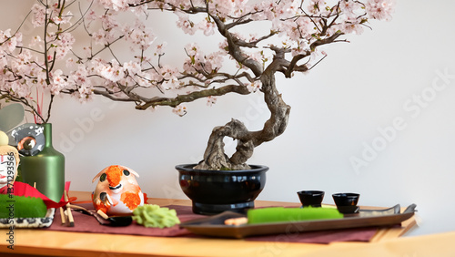 Japanese home with bonsai on a table with sushi, green tea, cherry blossoms in a vase and geisha.