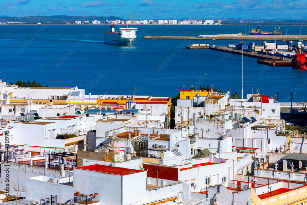 Bay of Cadiz showcasing charming contrast between whitewashed buildings and shimmering waters of bay beyond. Large ship is seen gliding towards bustling port, highlighting region active maritime life