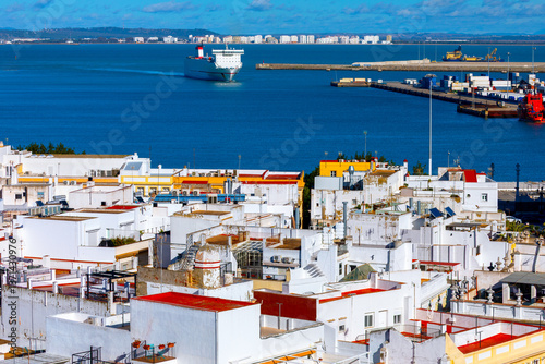 Obraz na płótnie Bay of Cadiz showcasing charming contrast between whitewashed buildings and shimmering waters of bay beyond. Large ship is seen gliding towards bustling port, highlighting region active maritime life w salonie