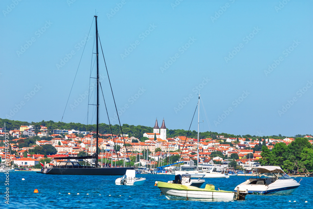 Charm of Medulin, Croatia, with stunning coastal scene featuring luxury yachts, sailboats and picturesque town with red-roofed houses. Crystal blue waters and serene harbor create Mediterranean escape