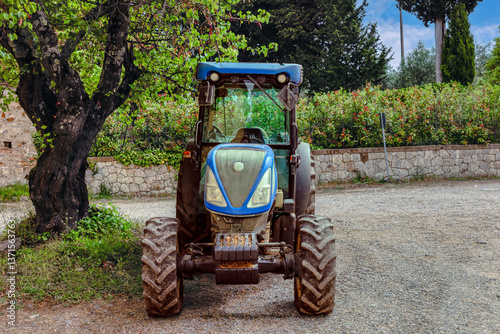 A blue tractor parked in a rustic setting under a tree in Toscana, Italy, showcasing rural life and agricultural activities
