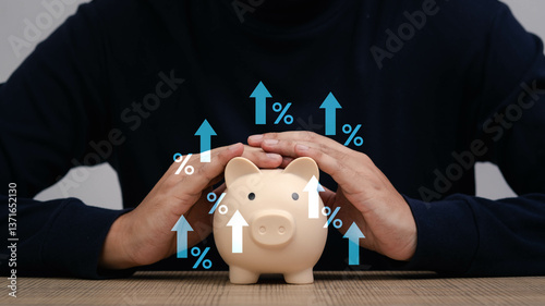 Fototapeta Naklejka Na Ścianę i Meble -  A person safeguarding a piggy bank with hands over it, symbolizing financial growth and savings with upward arrows and percentages around it.