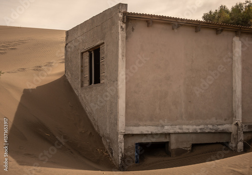 casa de dos pisos de construccion de ladrillo tapada en su totalidad por una duna de arena , 