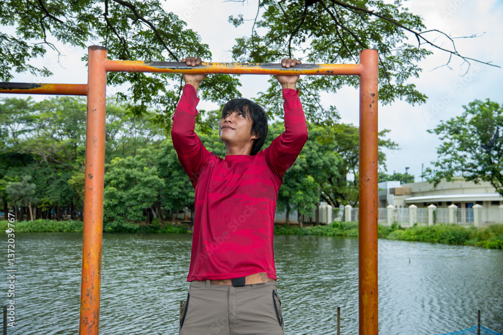 Fototapeta premium Strong man in red shirt doing pull-up exercise outdoors with lake background