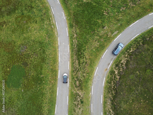 two roads with two cars heading in two directions within green mountain landscape with fresh grass