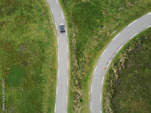 two roads with a car heading in two directions within green mountain landscape with fresh grass