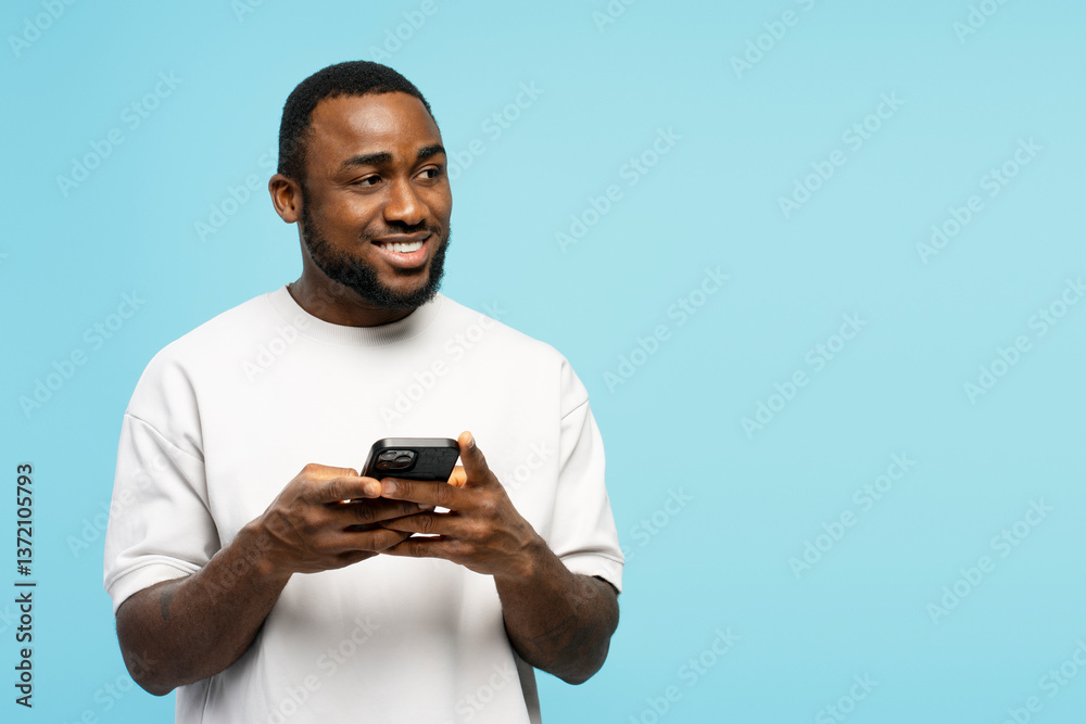 Smiling young African American man using smartphone on blue background Smiling young African American man using smartphone on blue background