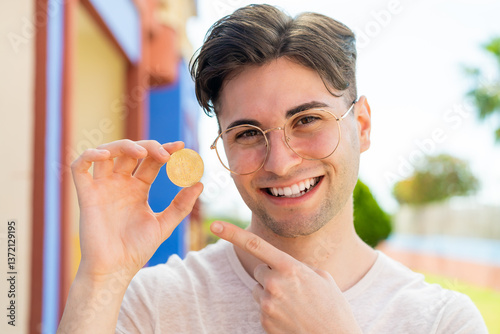 Wallpaper Mural Young handsome man holding a Bitcoin and pointing it Torontodigital.ca