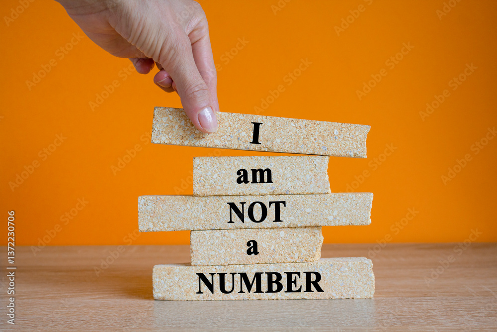 Concept words I am not a number written on brick blocks. Beautiful orange background, wooden table. Businessman hand. Business concept.