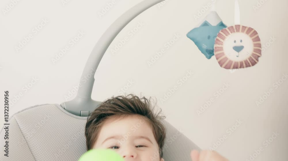Bright image of a baby enjoying playtime, holding a green ball while relaxing in a modern chair.