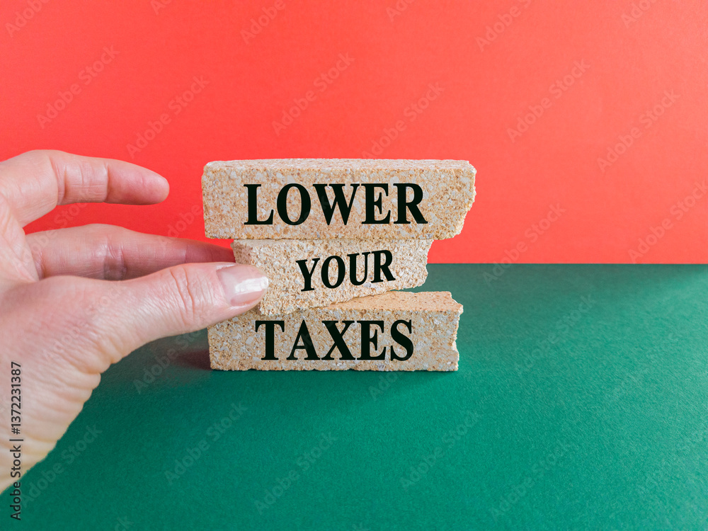 Lower your taxes symbol. Concept words Lower your taxes on brick blocks on a beautiful green table red background. Businessman hand. Business tax lower your taxes concept.
