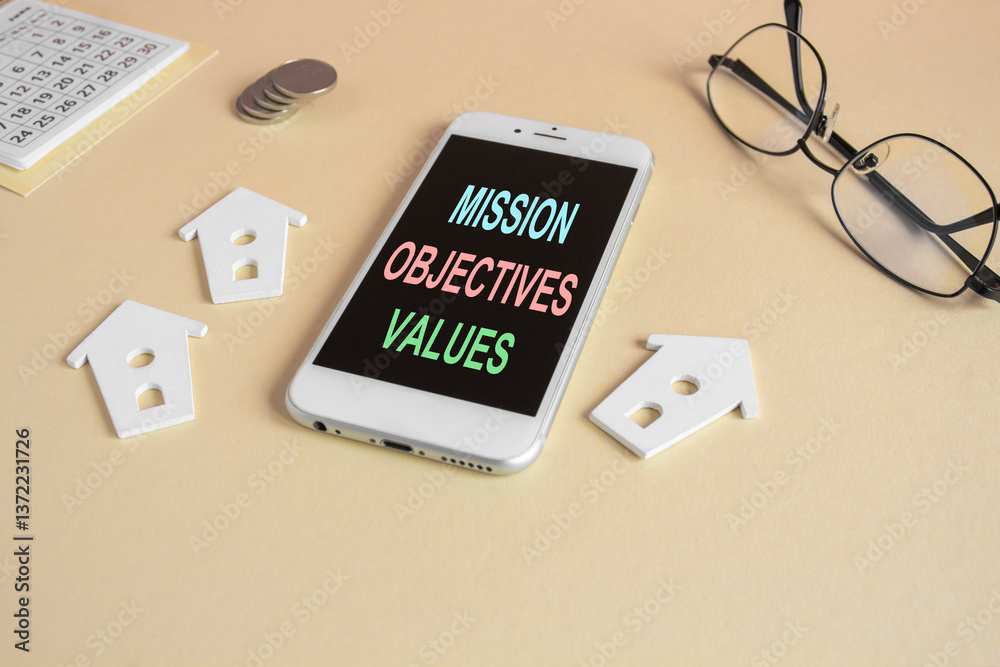 The expression Mission objectives values on the mobile phone screen. Beautiful beige background. Glasses, miniature houses, coins. Business concept.
