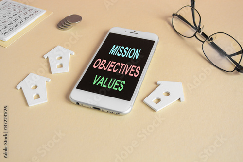 Obraz na płótnie The expression Mission objectives values on the mobile phone screen. Beautiful beige background. Glasses, miniature houses, coins. Business concept. w salonie