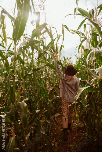 Portrait of young woman farmer inspecting corn field in summer sunny day.