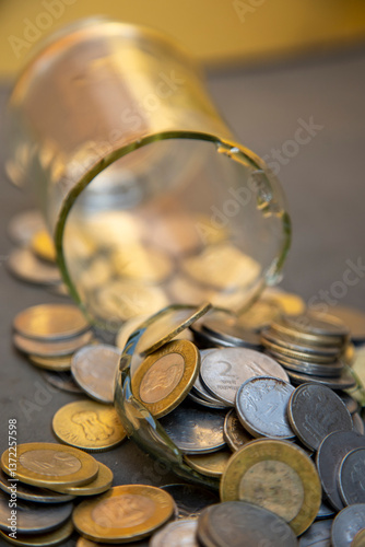 A broken glass jar with scattered coins symbolizes financial instability, economic hardship, or mismanaged savings. It represents themes of money loss, poverty, and financial struggles. photo