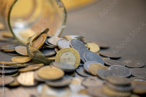 A broken glass jar with scattered coins symbolizes financial instability, economic hardship, or mismanaged savings. It represents themes of money loss, poverty, and financial struggles.