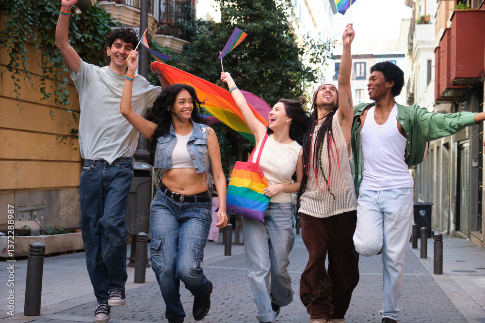 Group of happy multi ethnic friends running along a city street waving rainbow flags at a LGBT pride parade